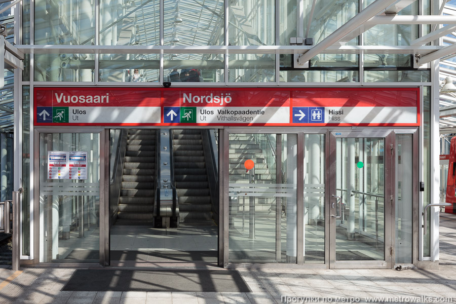 Станция Vuosaari / Nordsjö [Вуо́саа́ри] (Хельсинки). Выход в город, эскалаторы начинаются прямо с уровня платформы. Восточный выход на улицу Valkopaadentie — основной.