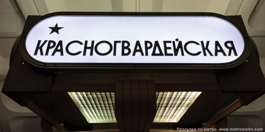 Станция Красногвардейская (Замоскворецкая линия, Москва). Название станции на светильниках-торшерах, установленных внутри скамеек по оси станции. Поскольку там внутри — лампы, освещающие ВСЮ станцию, смотреть на такой указатель больно.
