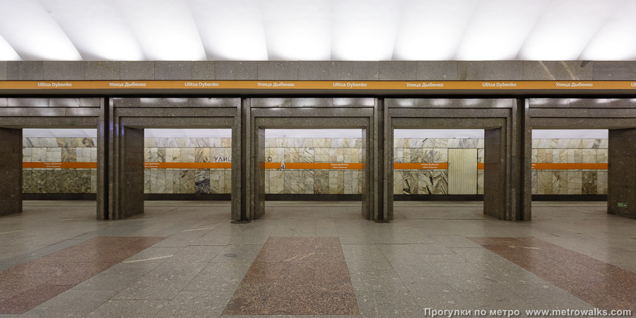Станция Улица Дыбенко (Правобережная линия, Санкт-Петербург). Поперечный вид, проходы между колоннами из центрального зала на платформу. Новая фотография, с оранжевой полосой.