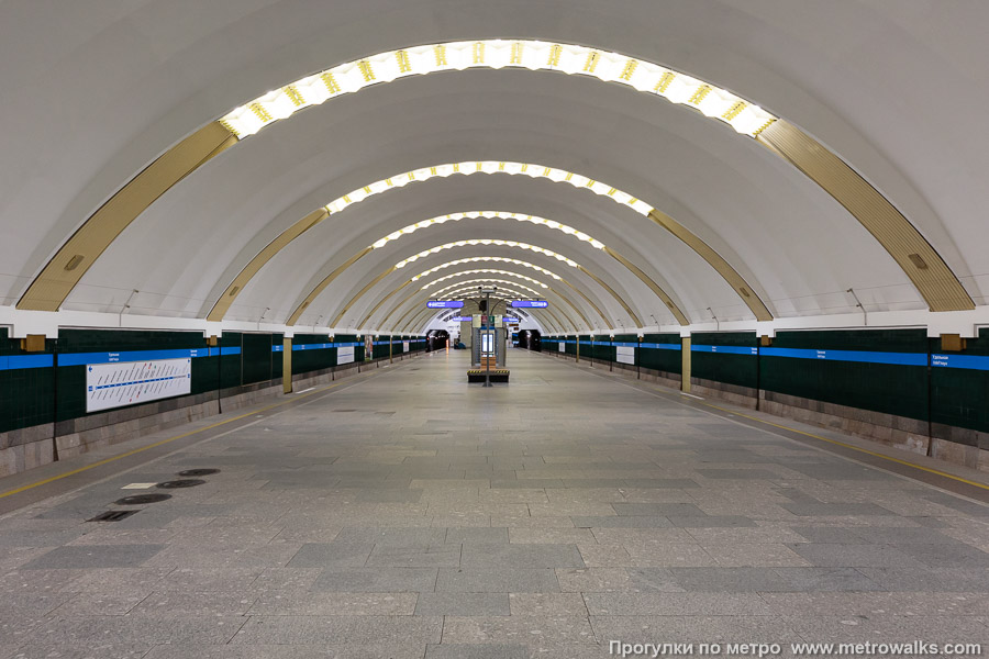 Станция Удельная (Московско-Петроградская линия, Санкт-Петербург). Общий вид по оси станции от входа в сторону глухого торца. Нагромождение лишних объектов на платформе полностью закрывает изначальную перспективу мемориала в дальнем торце.