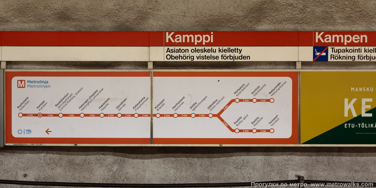 Фотография станции Kamppi / Kampen [Ка́мппи] (Хельсинки). Название станции на путевой стене и схема линии. Дополнительное сообщение гласит: «Бесцельное пребывание запрещено».