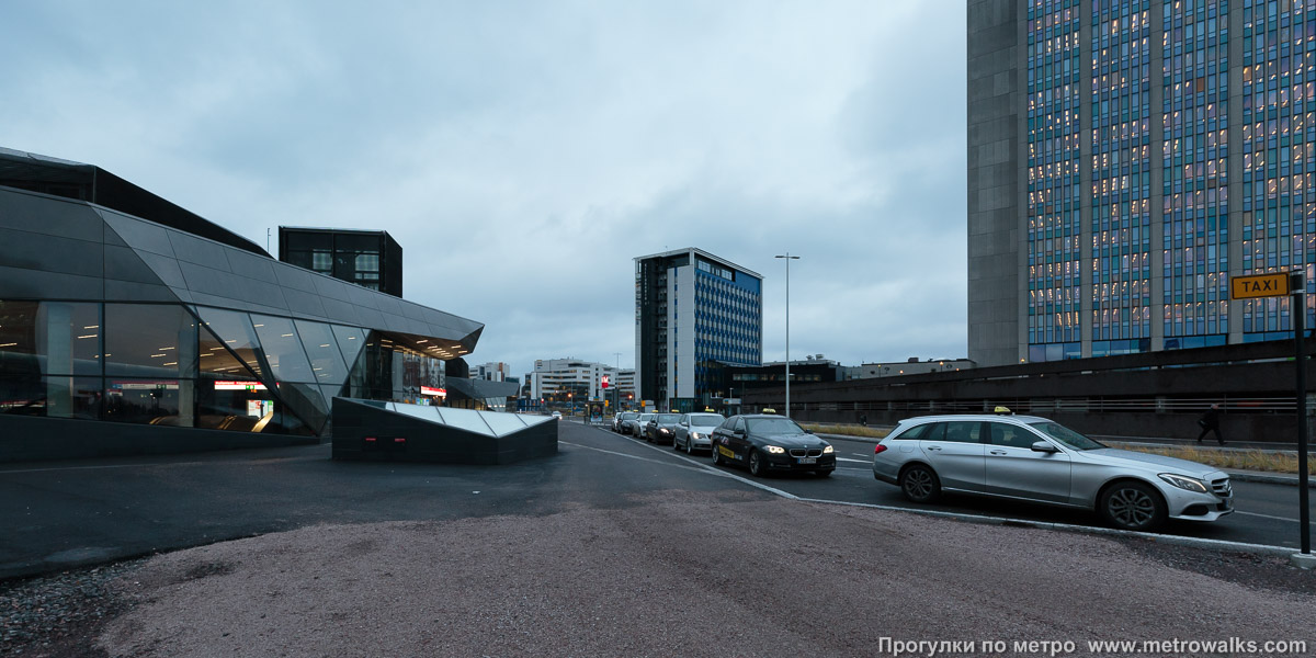 Фотография станции Keilaniemi / Kägeludden [Ке́йланиэ́ми] (Хельсинки). Общий вид окрестностей станции. На переднем плане — южный вестибюль «A», на заднем — северный «B», справа — небоскрёбы с офисами известных мировых корпораций.