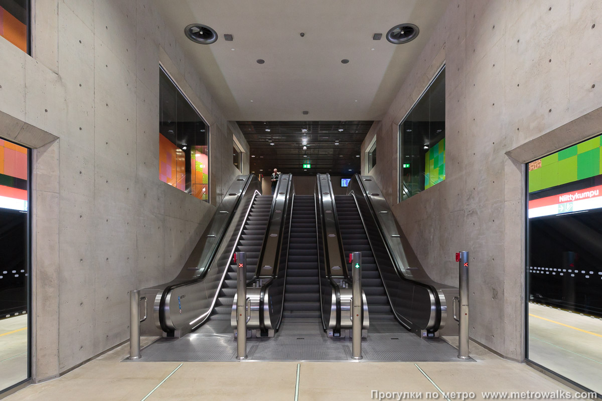 Фотография станции Niittykumpu / Ängskulla [Нии́ттюку́мпу] (Хельсинки). Выход в город, эскалаторы начинаются прямо с уровня платформы. За этими эскалаторами — переходный коридор к основной группе эскалаторов.