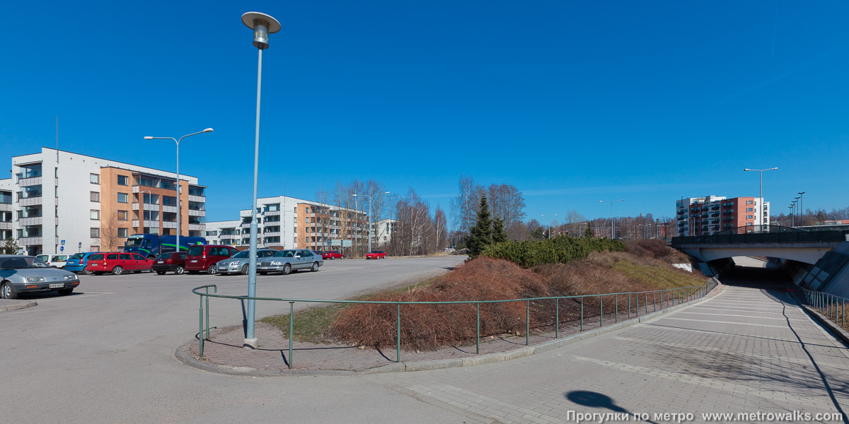 Фотография станции Puotila / Botby Gård [Пуо́тила] (Хельсинки). Общий вид окрестностей станции. Окрестности западного вестибюля с противоположной стороны шоссе Itäväylä, под которым проходит удобная пешеходная дорожка вдоль стеклянной стены станции.