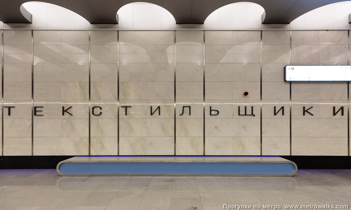 Фотография станции Текстильщики (Большая кольцевая линия, Москва). Название станции на станционной стене крупным планом. Из-за того, что шаг между декоративными полосами не кратен шагу букв, да ещё и не совпадает с разбивкой на слоги, кажется, что слово смонтировано вкривь-и-вкось.