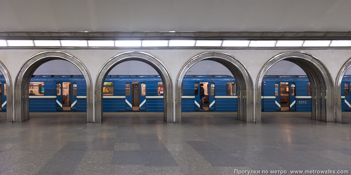 Фотография станции Академическая (Кировско-Выборгская линия, Санкт-Петербург). Поперечный вид, проходы между колоннами из центрального зала на платформу. Для разнообразия — с поездом.