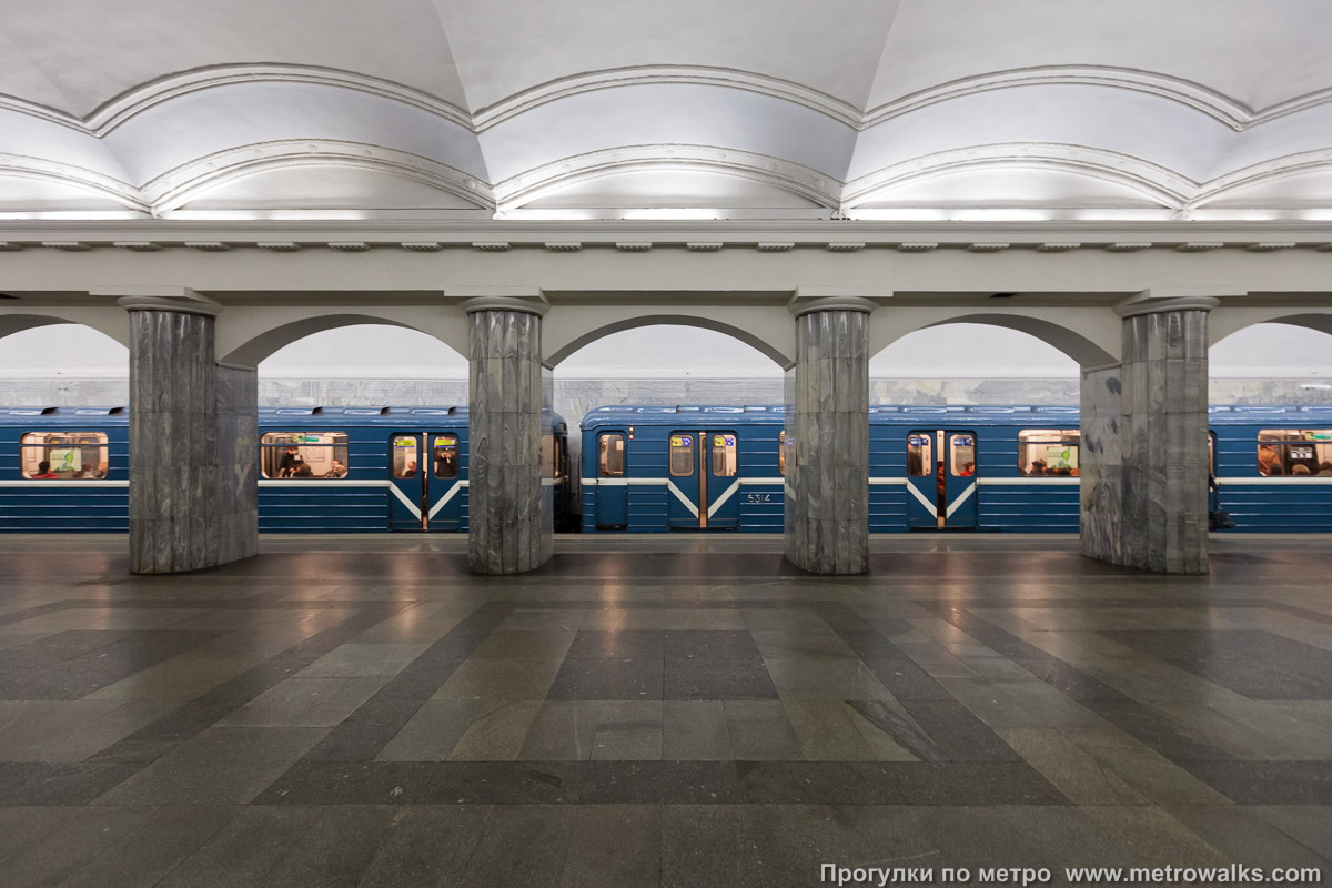 Фотография станции Балтийская (Кировско-Выборгская линия, Санкт-Петербург). Поперечный вид, проходы между колоннами из центрального зала на платформу. Для оживления картинки — с поездом.