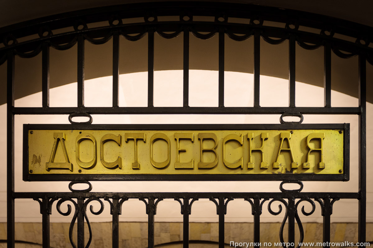 Фотография станции Достоевская (Правобережная линия, Санкт-Петербург). Декоративное оформление колонн крупным планом. Название станции «Достоевская» на решётке.