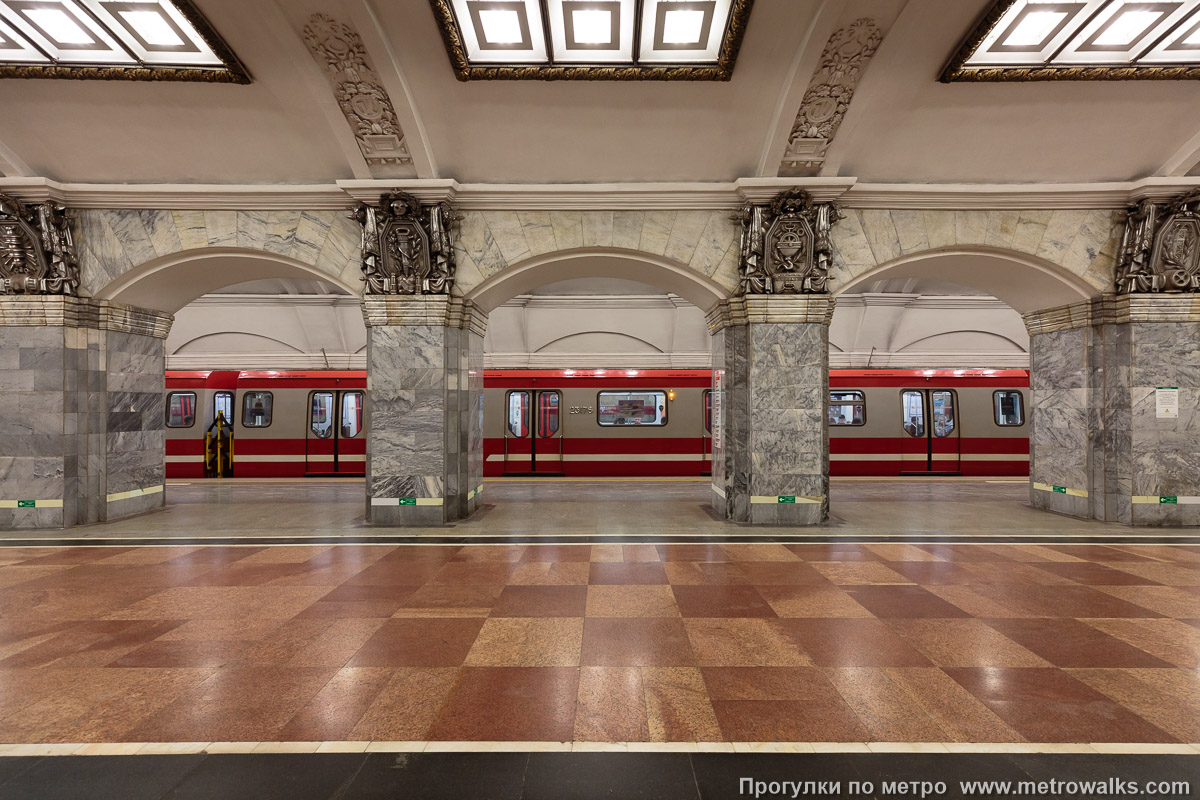 Фотография станции Кировский завод (Кировско-Выборгская линия, Санкт-Петербург). Поперечный вид, проходы между колоннами из центрального зала на платформу. Для пущей цветастости — с поездом.