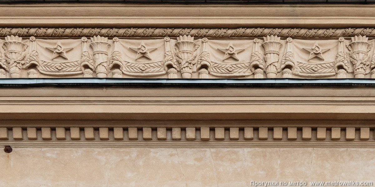 Фотография станции Кировский завод (Кировско-Выборгская линия, Санкт-Петербург). Архитектурное оформление вестибюля. Прикарнизный фриз с типовыми символами эпохи СССР — звёздами, серпами-и-молотами, знамёнами, факелами, дубовыми ветвями.