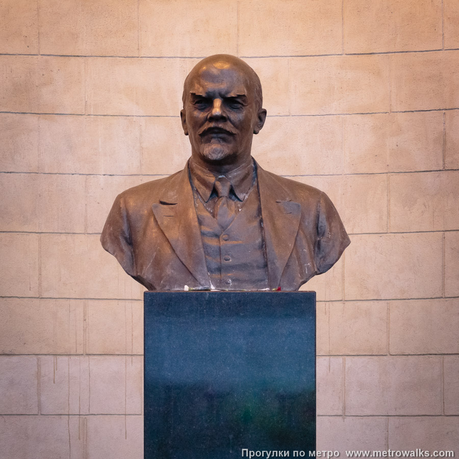 Фотография станции Кировский завод (Кировско-Выборгская линия, Санкт-Петербург). Декоративное оформление входа на станцию. Бюст В. И. Ленина (скульптор — Н. В. Дыдыкин), ранее стоявший в подземном зале станции, в 2026 был перенесён на улицу ко входу. Старый постамент из коричневого гранита был утрачен и заменён на чёрный.