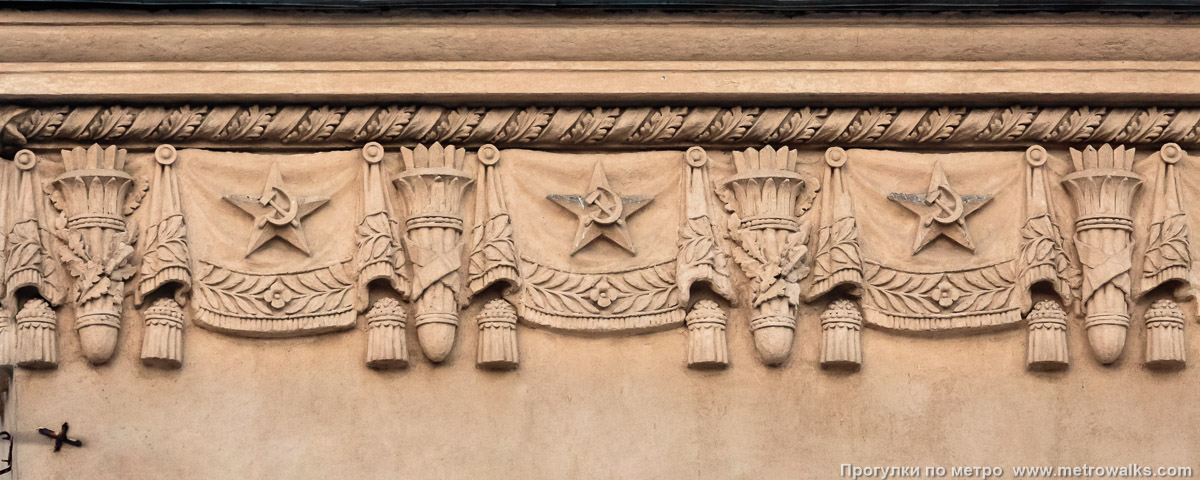 Фотография станции Кировский завод (Кировско-Выборгская линия, Санкт-Петербург). Архитектурное оформление вестибюля. Прикарнизный фриз с типовыми символами эпохи СССР — звёздами, серпами-и-молотами, знамёнами, факелами, дубовыми ветвями.