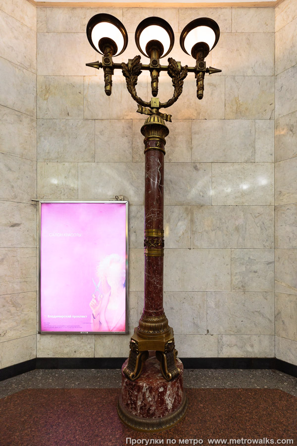 Фотография станции Владимирская (Кировско-Выборгская линия, Санкт-Петербург). Эскалаторный зал освещается высокими торжественными торшерами на ножках из красного мрамора, украшенными звёздами, дубовыми венками и другими литыми деталями.