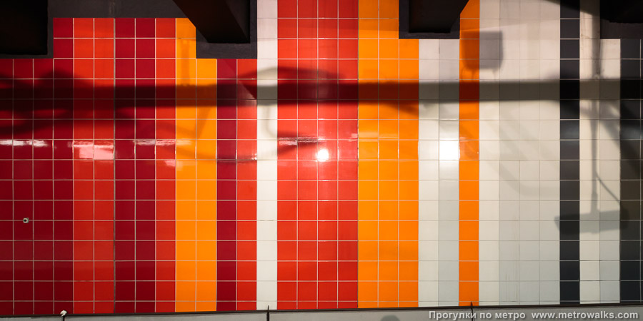 Станция Roi Baudouin / Koning Boudewijn [Руа́ Бодуэ́н / Конинг Баудэвейн] (линия 2/6, Брюссель). Декоративное оформление путевой стены крупным планом. Красный и оранжевый.