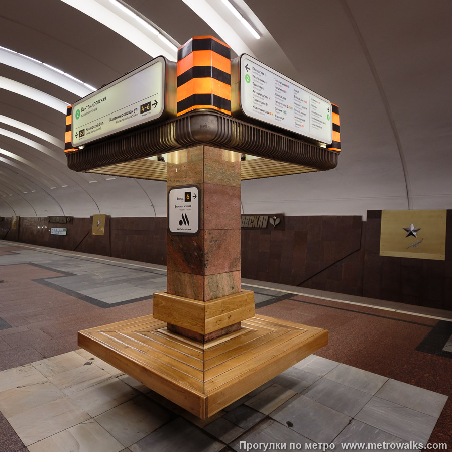 Станция Кантемировская (Замоскворецкая линия, Москва). Скамейки, совмещённые с указателями. Углы торшеров украшены вставками в стиле Гвардейской ленты — с чёрными и оранжевыми полосами.