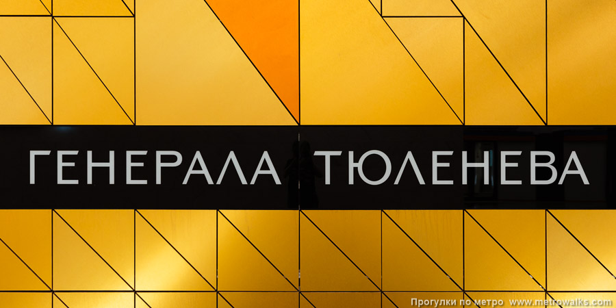 Станция Генерала Тюленева (Троицкая линия, Москва). Название станции на путевой стене крупным планом. На однотонном оранжевом фоне.