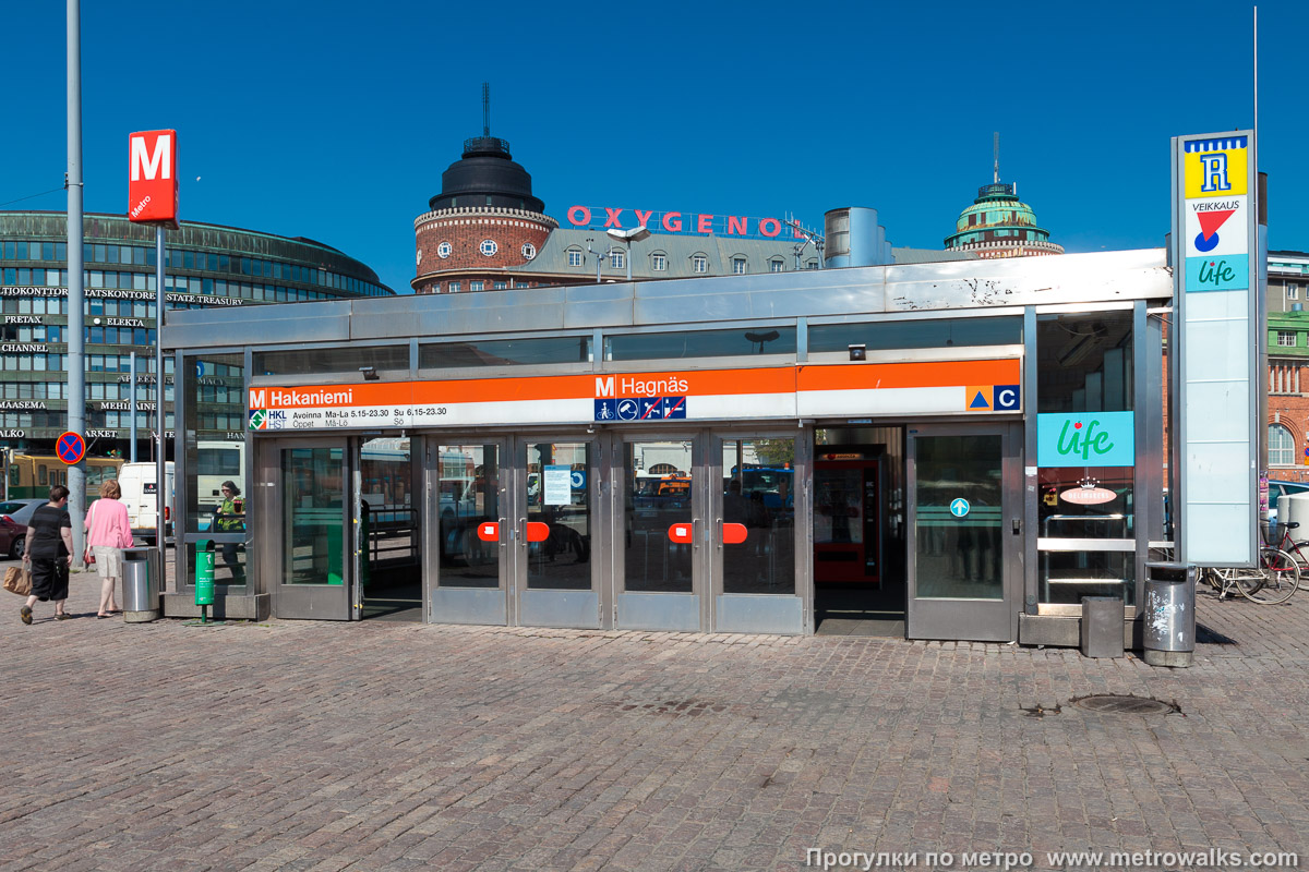 Фотография станции Hakaniemi / Hagnäs [Ха́каниэ́ми] (Хельсинки). Вход на станцию осуществляется через подземный переход. Ещё один спуск в подземный переход в центре площади.