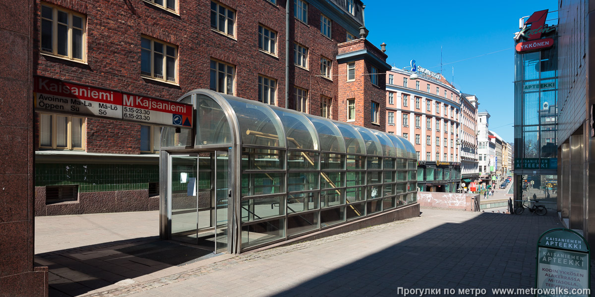 Фотография станции Helsingin yliopisto / Helsingfors universitet [Хе́льсиньин у́лио́писто] (Хельсинки). Вход на станцию осуществляется через подземный переход. Дополнительный вход с Горной улицы — Vuorikatu. Основной вход — на заднем плане внизу.