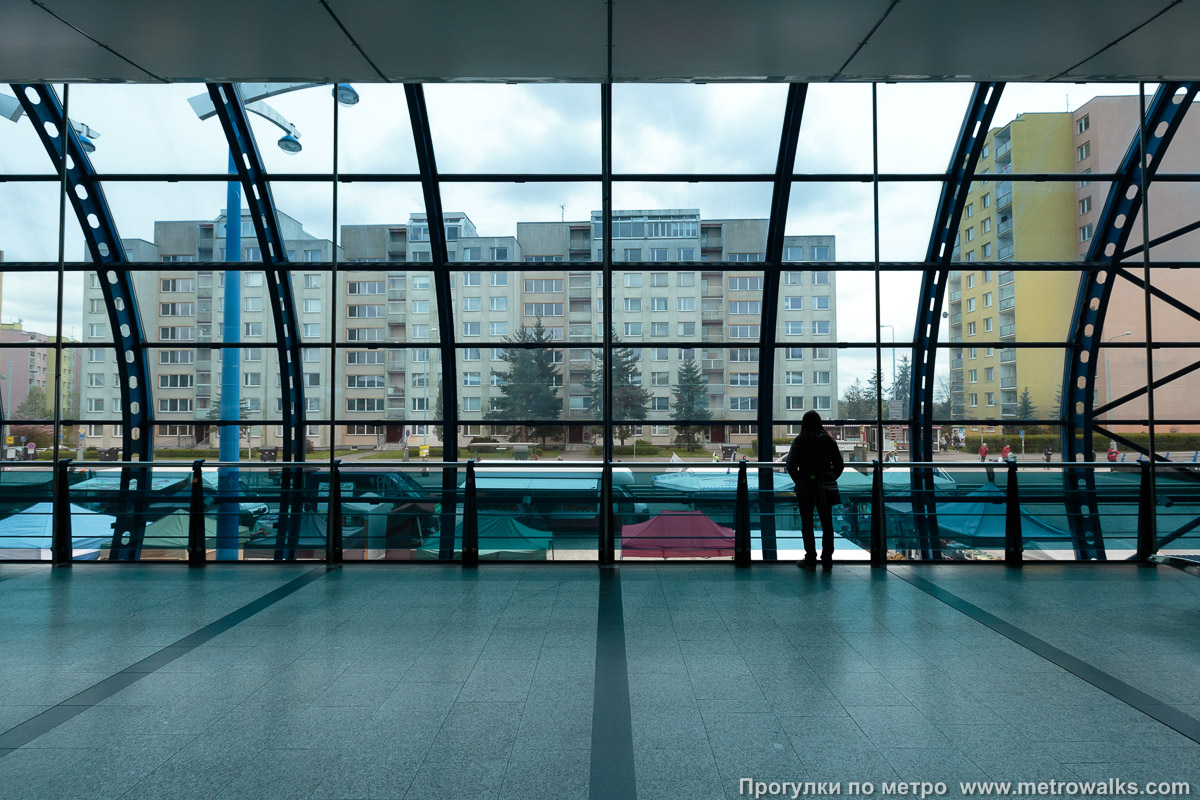 Фотография станции Rajská zahrada [Райска заграда] (линия B, Прага). Поперечный вид. Сквозь стеклянную стену открывается панорамный вид окружающего микрорайона.