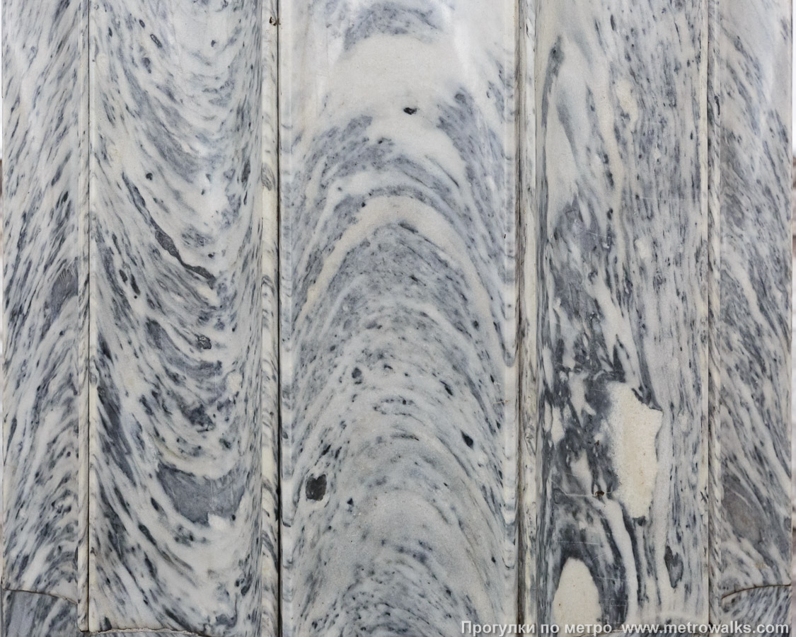 Фотография станции Балтийская (Кировско-Выборгская линия, Санкт-Петербург). Со стороны центрального зала облицовка колонн выполнена с полукруглыми бороздками, что превратило прямые прожилки мрамора в изгибающиеся, как бегущие волны Балтийского моря.