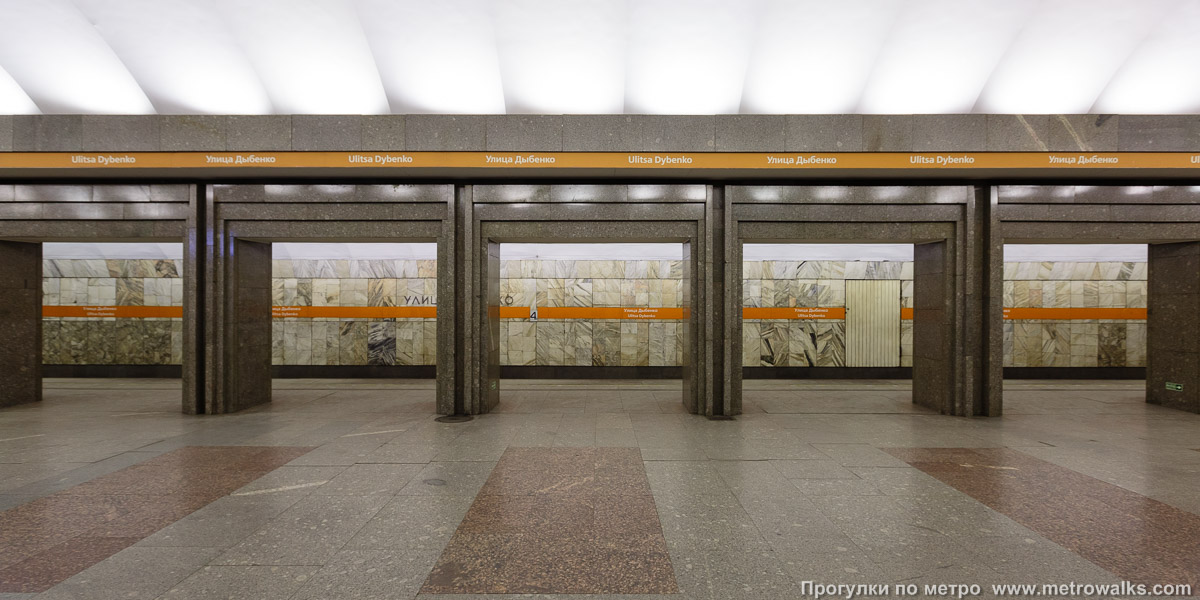 Фотография станции Улица Дыбенко (Правобережная линия, Санкт-Петербург). Поперечный вид, проходы между колоннами из центрального зала на платформу. Новая фотография, с оранжевой полосой.