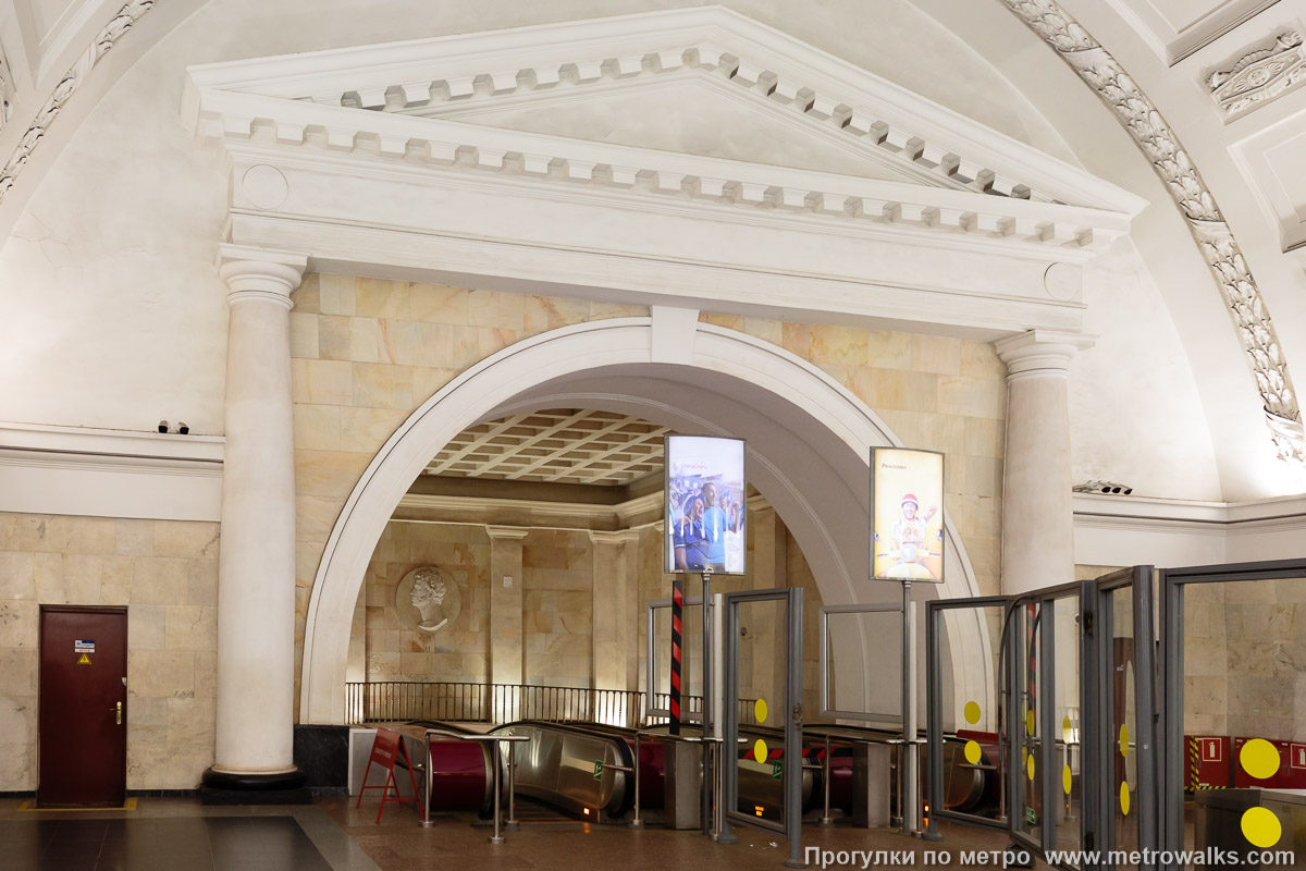 Фотография станции Пушкинская (Кировско-Выборгская линия, Санкт-Петербург). Эскалаторный спуск расположен в прямоугольной апсиде, отделённой от основного зала полукруглым порталом с треугольным фронтоном.