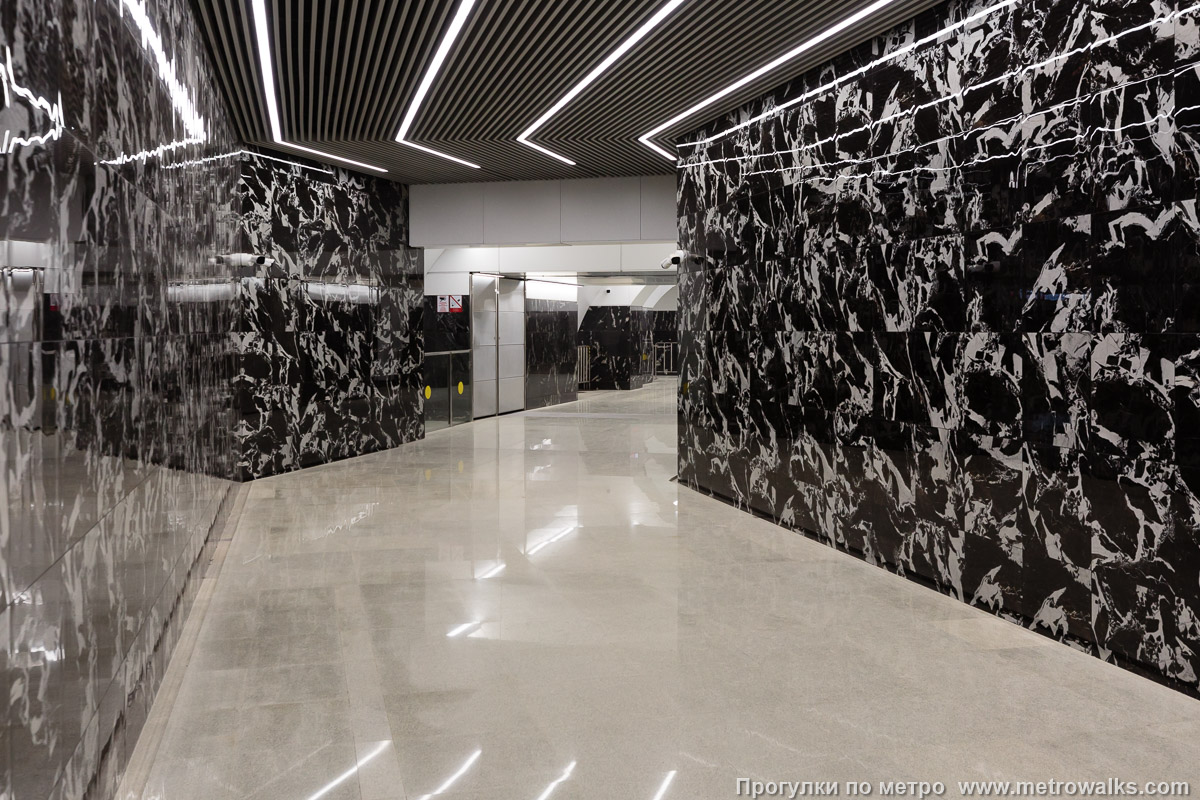 Фотография станции Путиловская (Красносельско-Калининская линия, Санкт-Петербург). Узкий коридор перехода от Путиловской к эскалаторам на Кировский завод. Вместо плавной дуги был построен в современном московском стиле со множеством резких угловатых поворотов: прямо их два, и ещё один — за спиной фотографа.