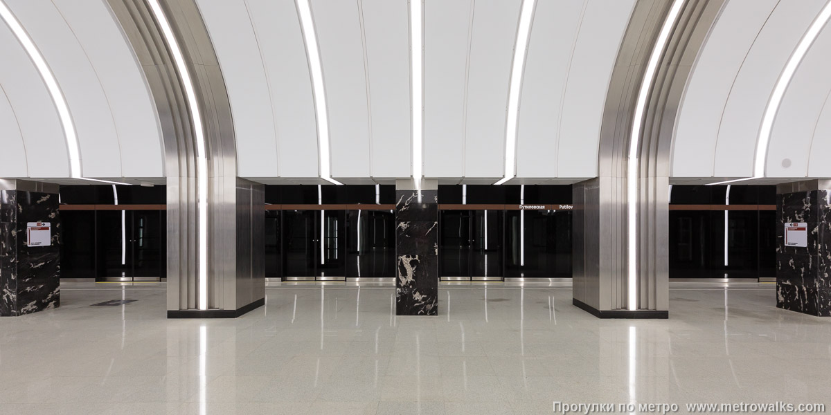 Фотография станции Путиловская (Красносельско-Калининская линия, Санкт-Петербург). Поперечный вид, проходы между колоннами из центрального зала на платформу. Чередование отделочных материалов соседних колонн лишает колоннаду строгости и классического торжественного вида.