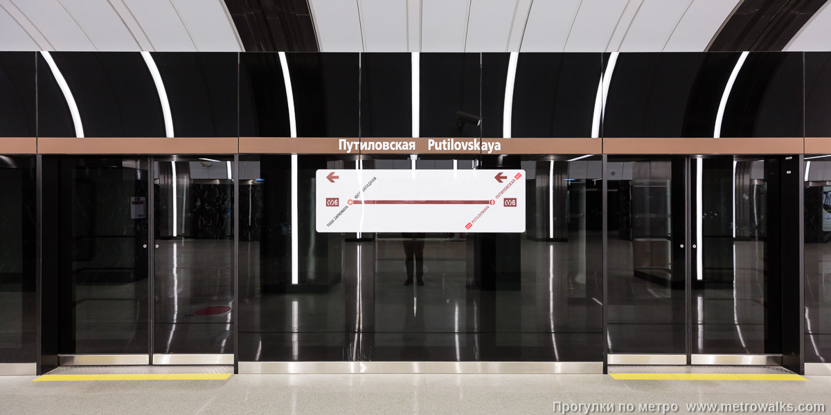 Фотография станции Путиловская (Красносельско-Калининская линия, Санкт-Петербург). Станционная стена. Поскольку стеклянная стенка почти непрозрачная, путевая стена за ней оставлена без декоративной отделки, что можно разглядеть через окна поезда.