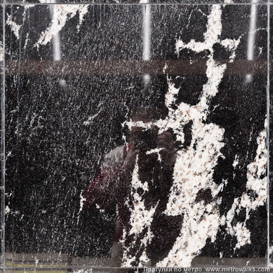 Фотография станции Путиловская (Красносельско-Калининская линия, Санкт-Петербург). Фрагмент облицовки колонны крупным планом. Контрастный чёрно-белый амфиболит на колоннах выглядит уместно, как предупреждение о препятствии. Но на стеновых вставках между колоннами рябит в глазах от избытка контрастных полос, там лучше смотрелся бы нейтральный камень.