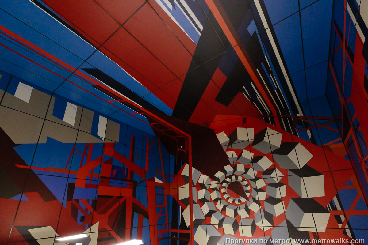 Фотография станции Путиловская (Красносельско-Калининская линия, Санкт-Петербург). Декоративное оформление стены над спуском. Левая сторона. К сожалению, прямой ракурс перекрыт неудачно высоко расположенными стойками светильников.