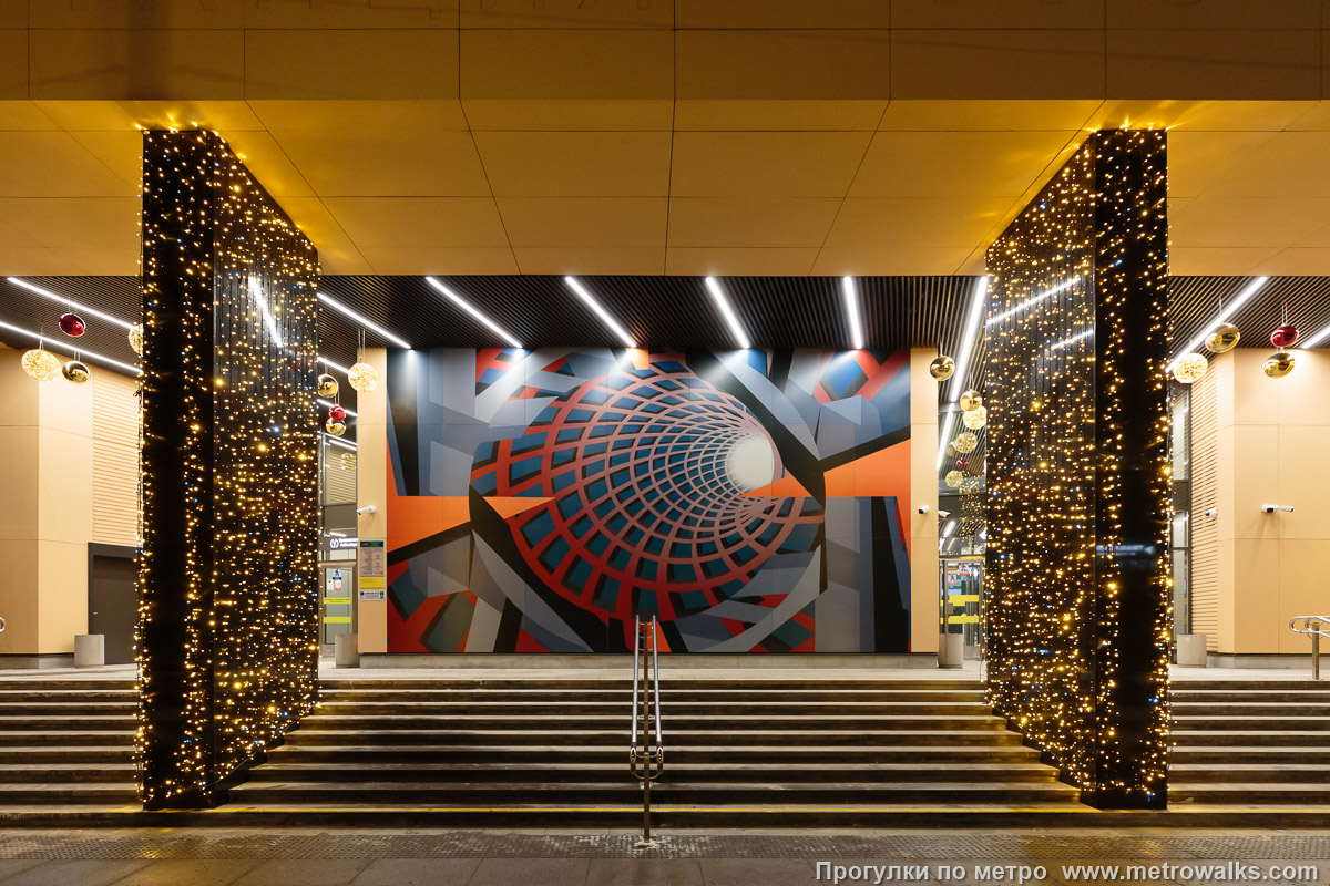 Фотография станции Путиловская (Красносельско-Калининская линия, Санкт-Петербург). Главный фасад здания наземного вестибюля станции. Массивные колонны прямоугольного сечения установлены под разными углами. Подсветка была временным украшением в дни открытия станции, впоследствии демонтирована.