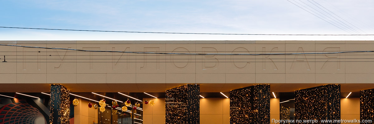 Фотография станции Путиловская (Красносельско-Калининская линия, Санкт-Петербург). Название станции на здании вестибюля. Архитектор просчитался: название совершенно не контрастно даже при солнечном свете, и практически невозможно найти точку зрения, откуда оно было бы видно не будучи перекрытым проводами (кроме как ровно с середины проезжей части).