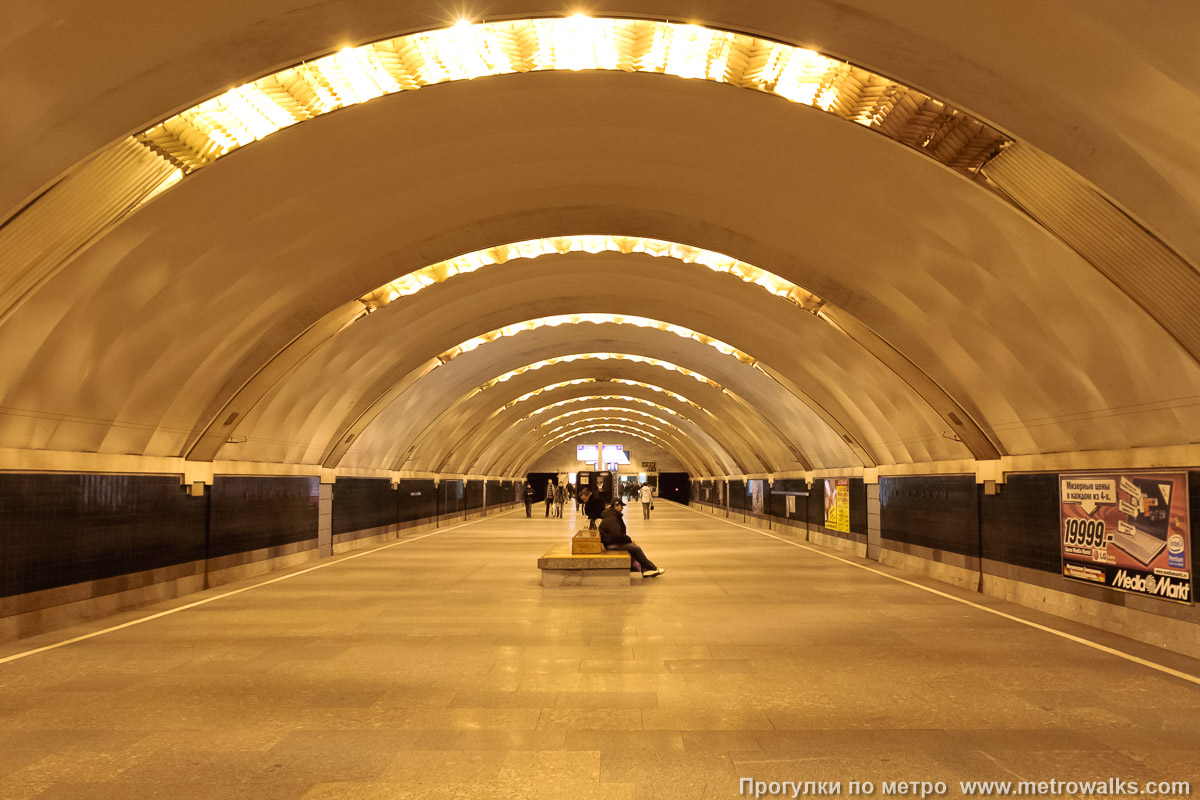 Фотография станции Удельная (Московско-Петроградская линия, Санкт-Петербург). Общий вид по оси станции от глухого торца в сторону выхода. Старая фотография (2008), до наклеивания синей полосы на стену.