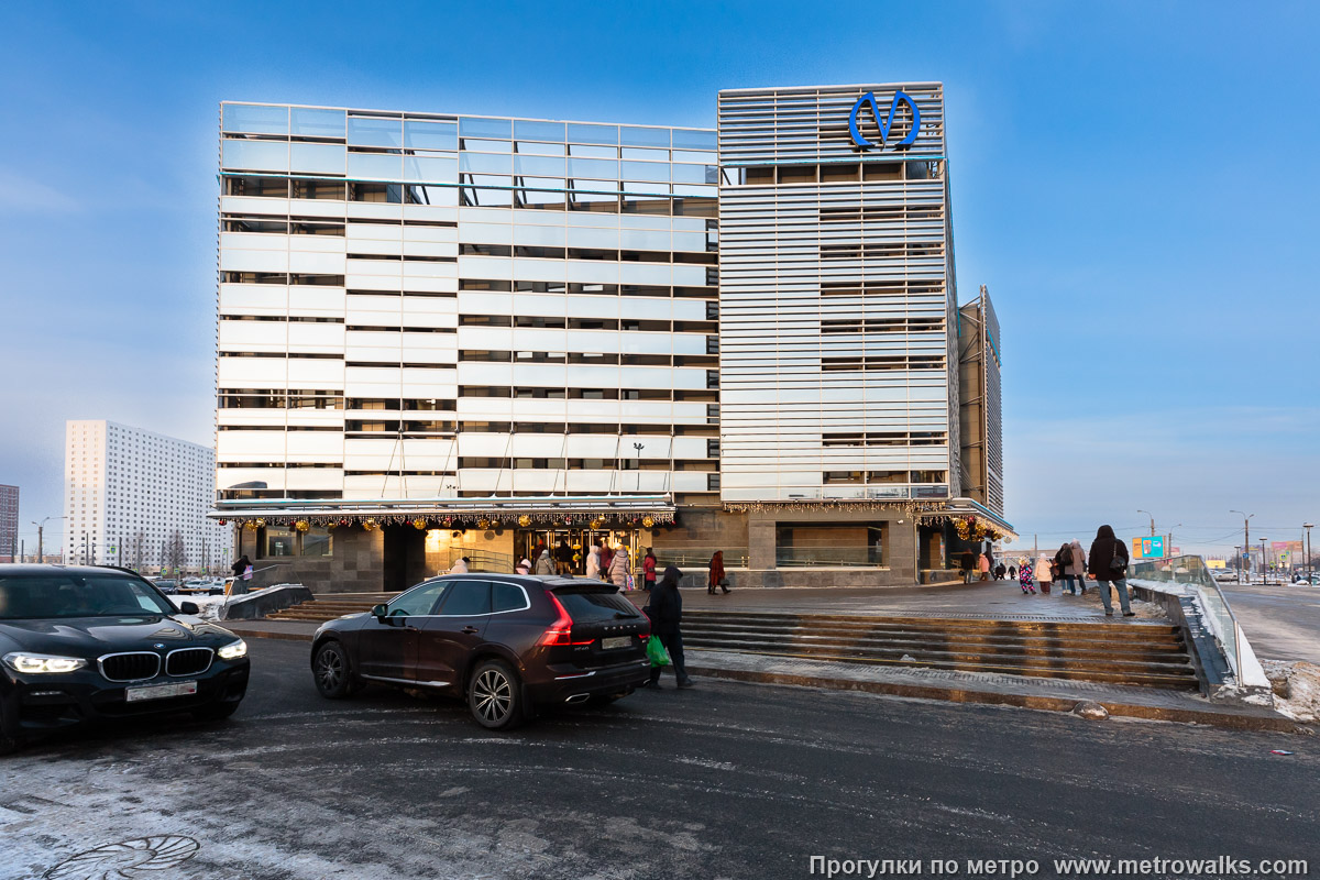 Фотография станции Юго-Западная (Красносельско-Калининская линия, Санкт-Петербург). Тот же вестибюль, вид сбоку. Спуск со стилобата прямо у основных дверей выхода ведёт непосредственно на проезжую часть парковки соседнего гипермаркета без какого-либо промежуточного тротуара.